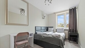A bedroom with a bed, a desk, a chair, a mirror, and a window with curtains. - RentPlanet - Apartament na Śródmieściu (Warsaw)