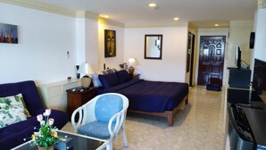 A hotel room with a bed, a chair, a table with flowers, a lamp, and a TV. - Spacieux Studio, Tres Belle vue mer sur la Baie de Patong (Tambon Patong)