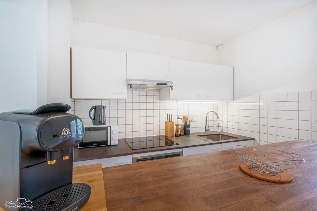 Une cuisine moderne avec des meubles blancs, une machine à café noire, un évier et un plan de travail en bois.