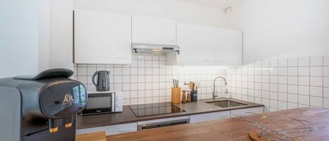 Une cuisine moderne avec des meubles blancs, une machine à café noire, un évier et un plan de travail en bois.