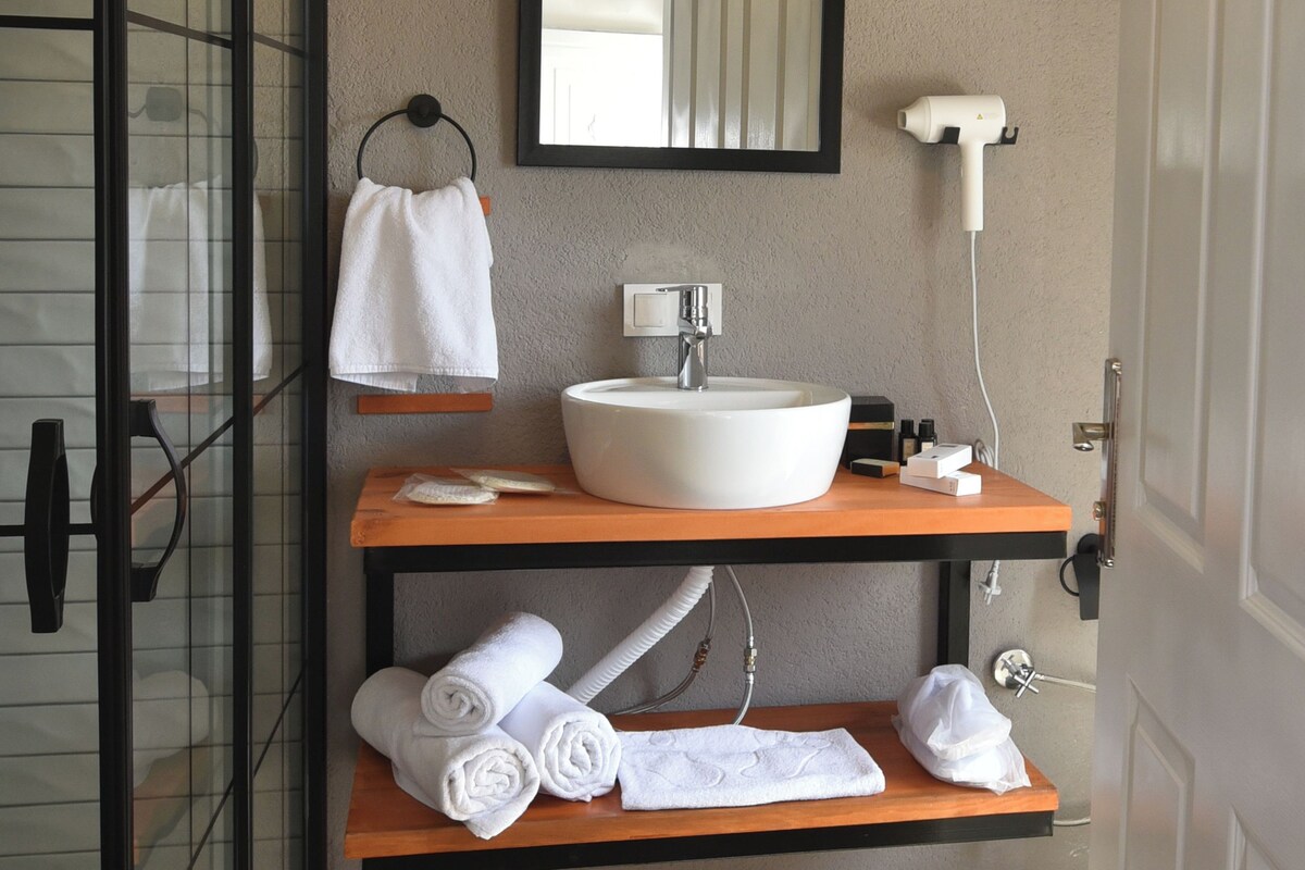 Un baño con cabina de ducha de vidrio, un lavabo blanco, un espejo y un perchero para toallas.