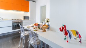 A modern kitchen with white and orange cabinets, a dining area with clear chairs, and a decorative animal sculpture. - House "The Seagull" with garden/ grill/ jacuzzi sea view (Bordighera)