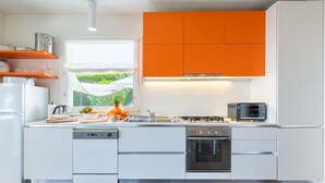 A modern kitchen with white cabinets, an orange accent wall, a window with a view of greenery, a built-in oven, and a gas stove. - House "The Seagull" with garden/ grill/ jacuzzi sea view (Bordighera)