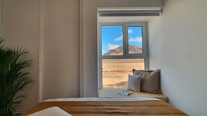 Quarto com cama, janela com vista para paisagem desértica e planta em vaso.