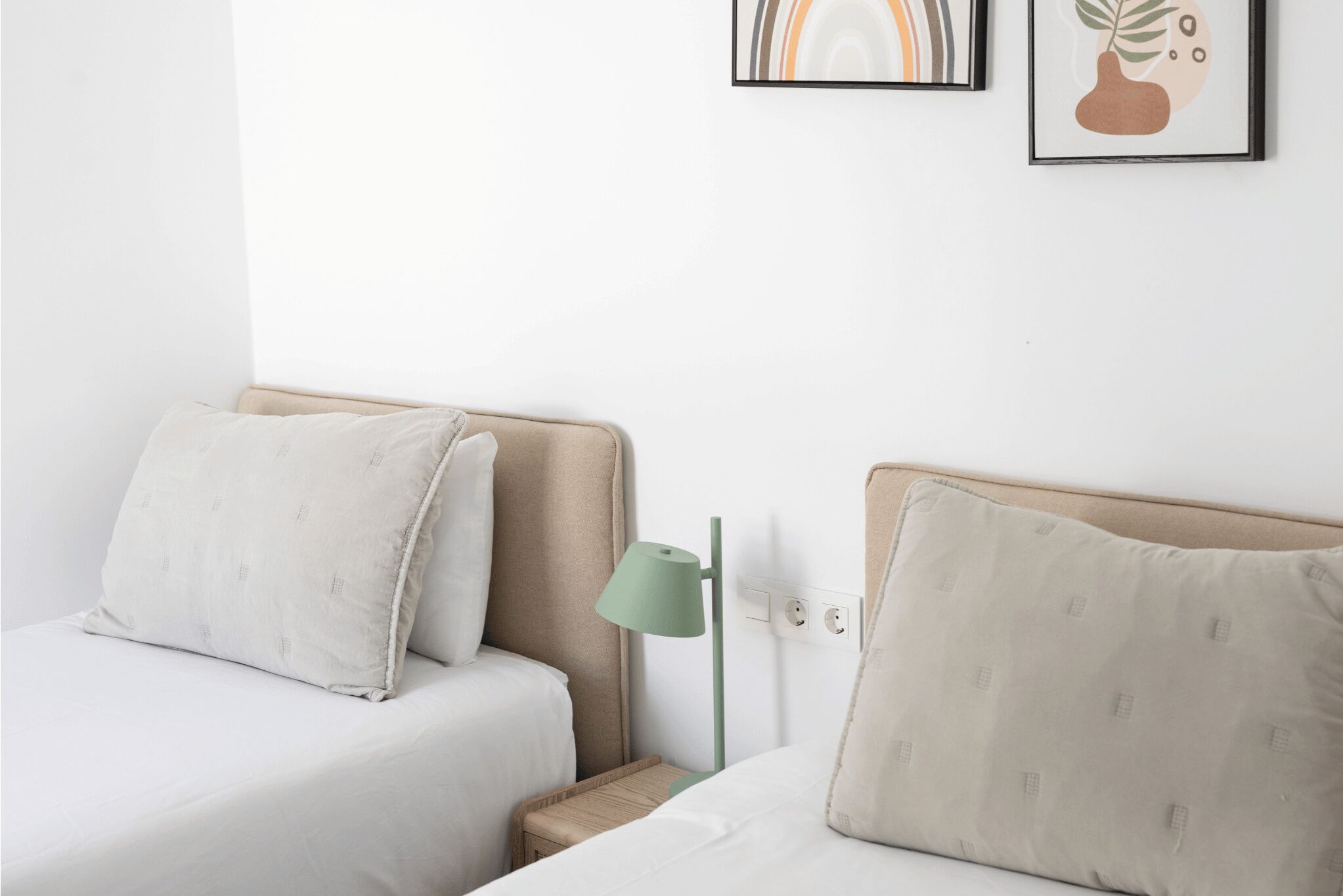 Een hotelkamer met twee bedden, een nachtkastje, een lamp en twee ingelijste foto’s aan de muur.