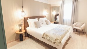 A modern hotel room with a large bed, bedside tables, a chair, and a mirror.