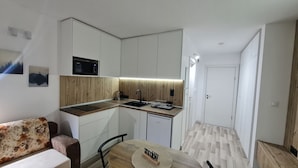 Cocina compacta con microondas, pileta y encimera de madera. Hay un comedor con mesa y sillas.
