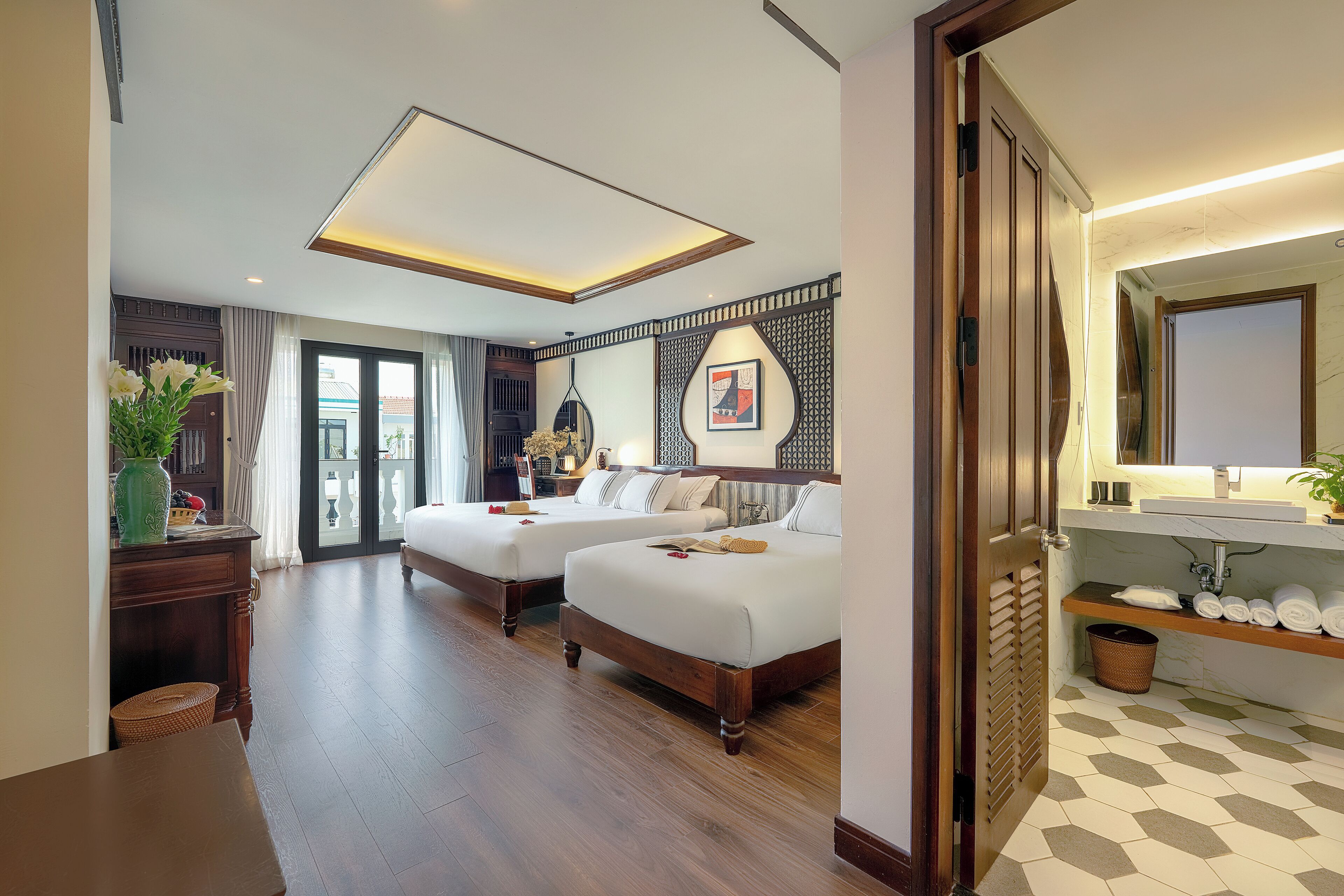 A hotel room with two beds, a wooden desk, a mirror, and a bathroom with a sink and towel rack.
