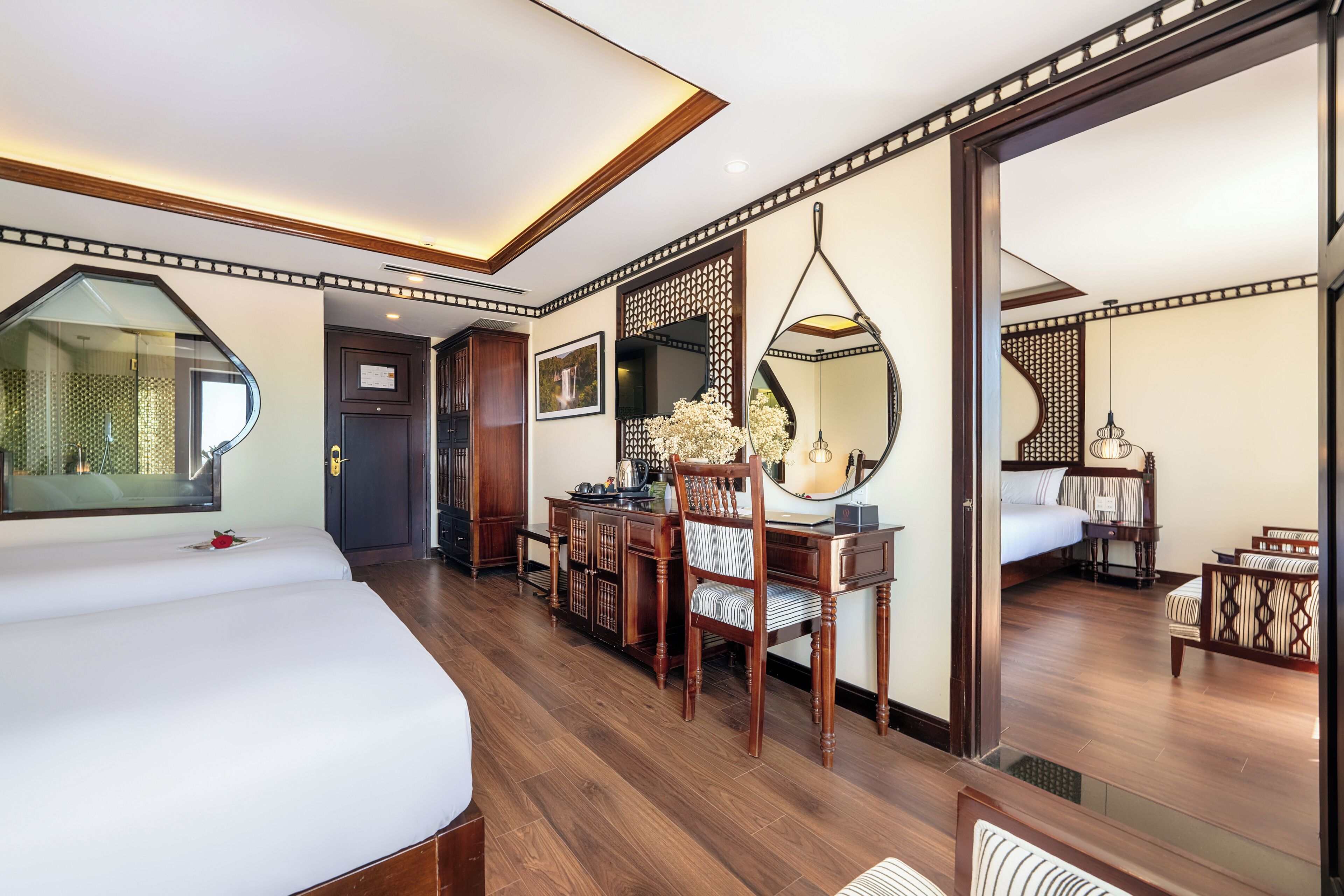 A hotel room with a large bed, a desk with a chair, a mirror, and a wardrobe.