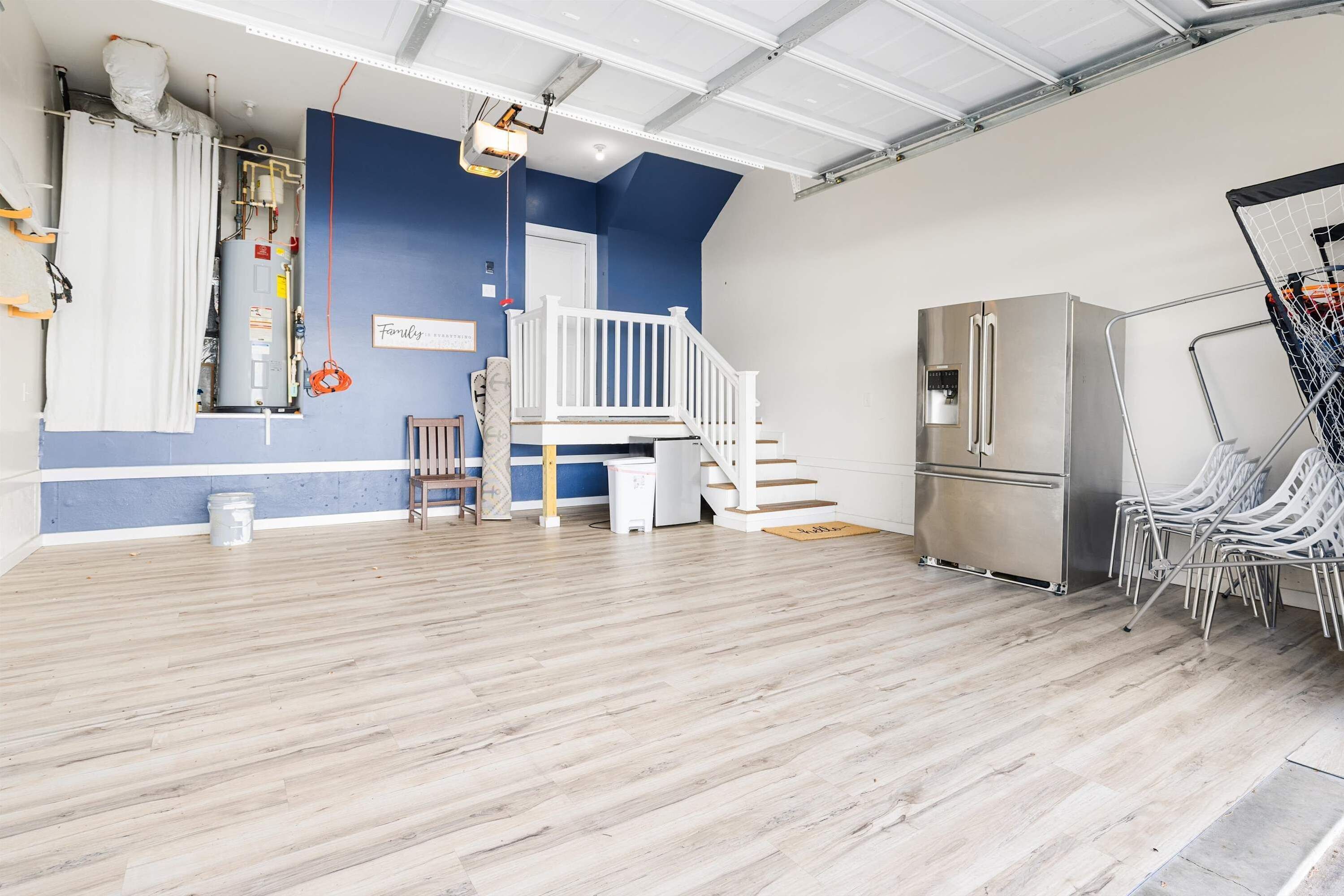 Une pièce spacieuse avec un plancher en bois, un escalier blanc, une rampe blanche, un réfrigérateur en acier inoxydable et un panier de basket.