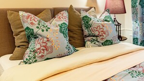 Cama bem arrumada com almofadas estampadas e colcha de cor clara. Há quadros emoldurados na parede acima da cama.