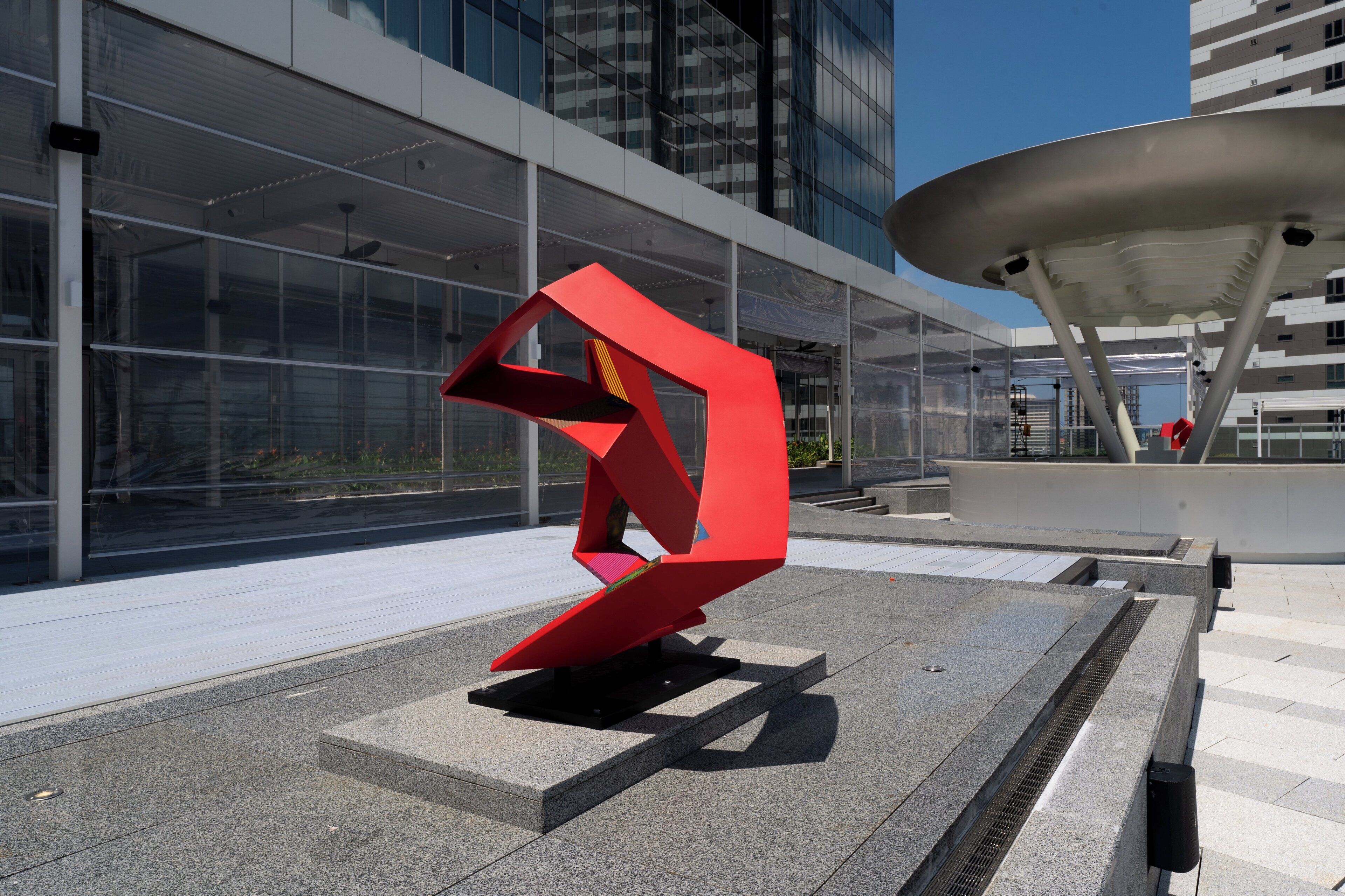 A modern building with a glass facade and a red abstract sculpture in the foreground.