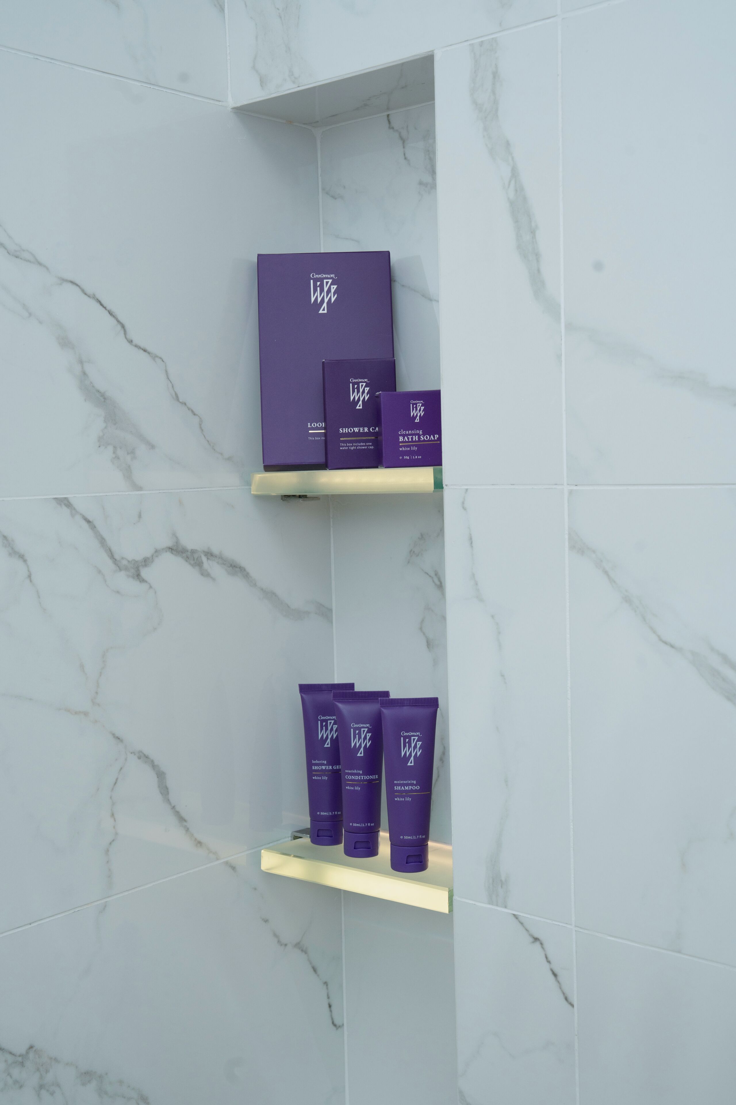 A bathroom with marble walls and shelves holding various toiletries.