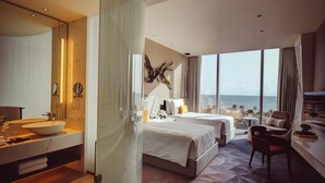 A modern hotel room with a large bed, a sitting area, a bathroom with a large mirror, and a view of the ocean.