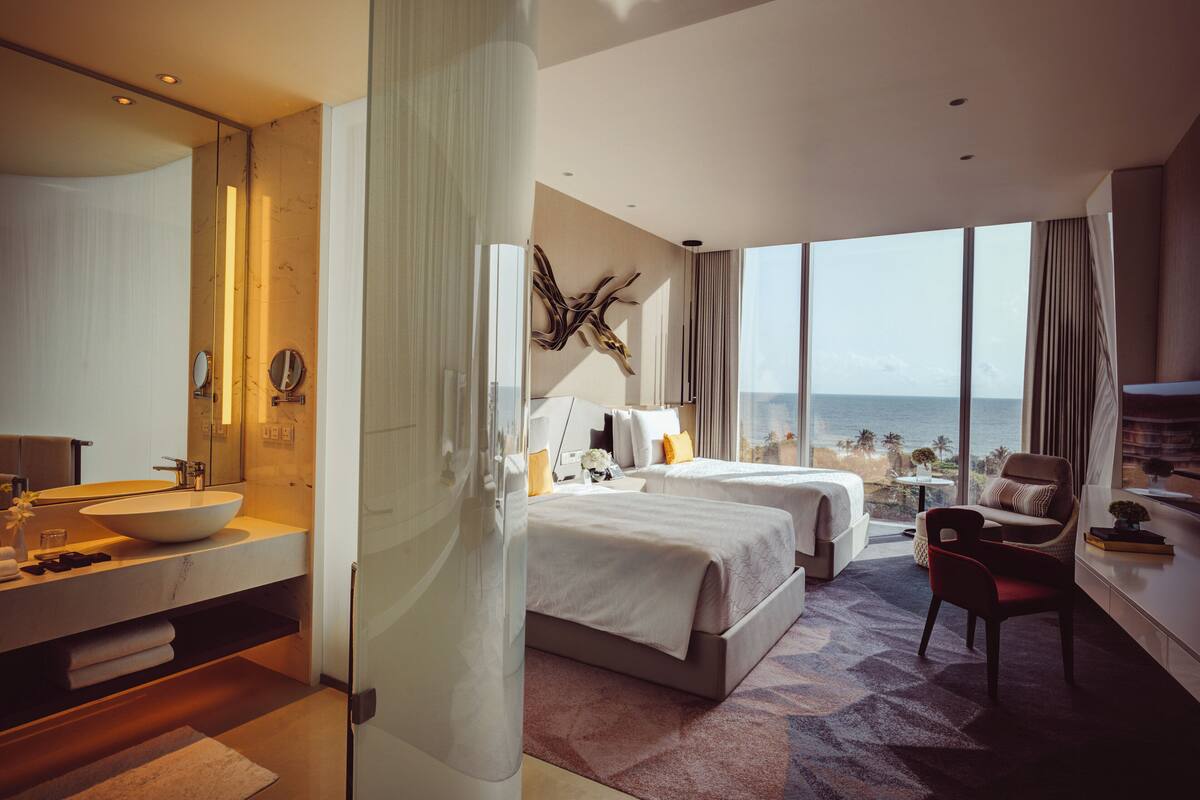 Una camera d'albergo moderna con un letto grande, un angolo salotto, un bagno con uno specchio ampio e vista sull'oceano.