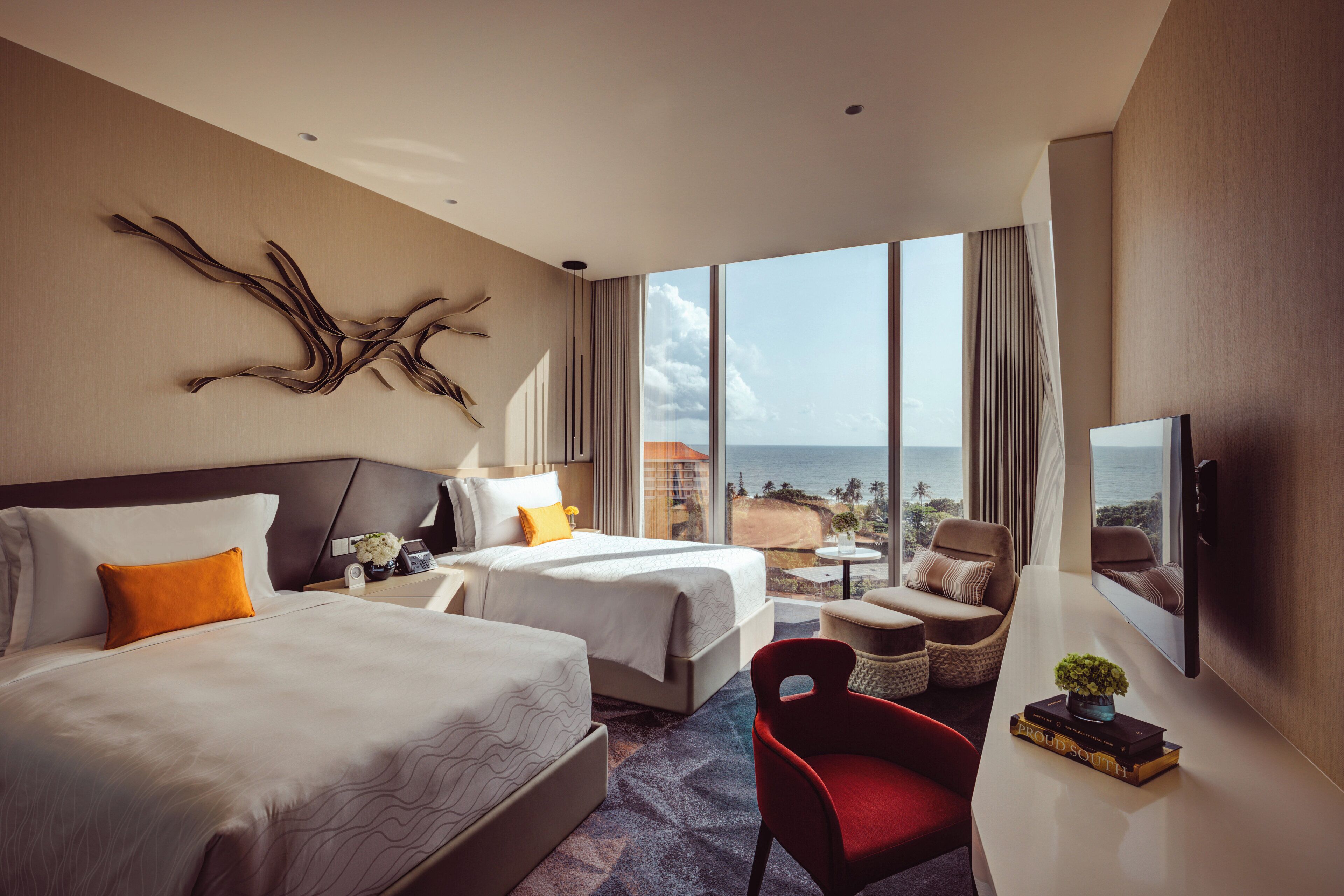 Habitación de hotel con dos camas, un escritorio, una silla y un ventanal con vista al océano.