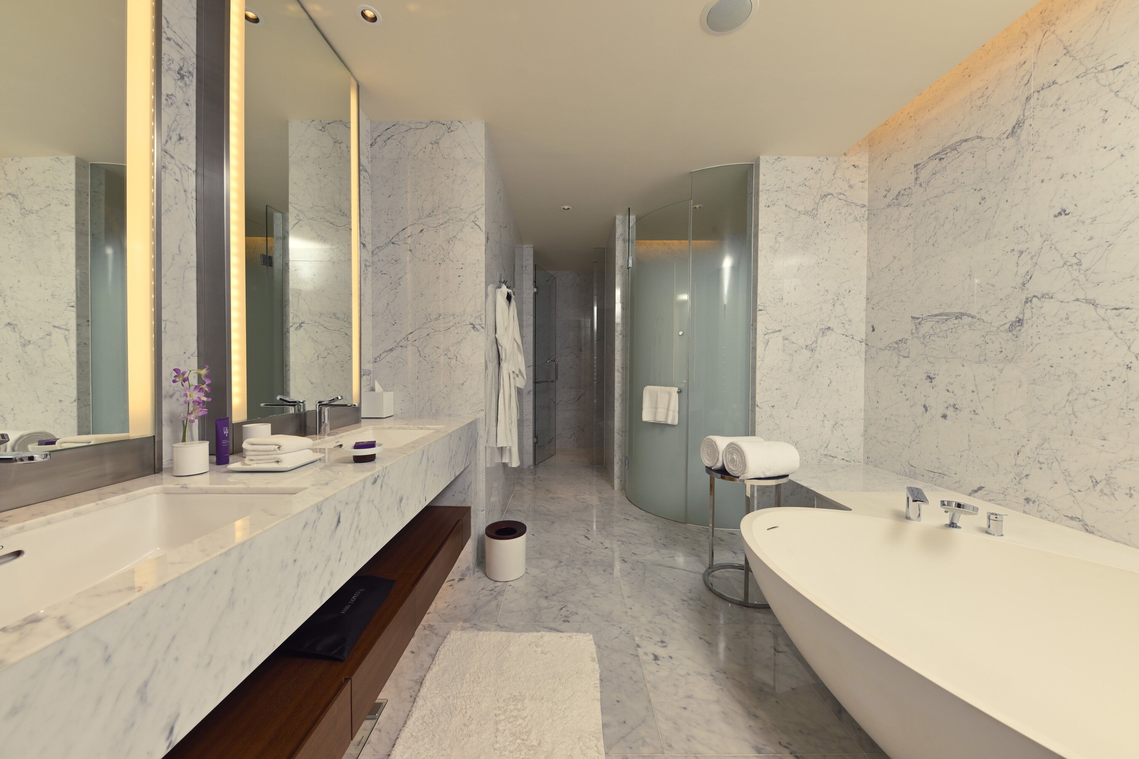Un baño moderno con un espejo grande, dos lavamanos, una bañera y paredes de mármol.
