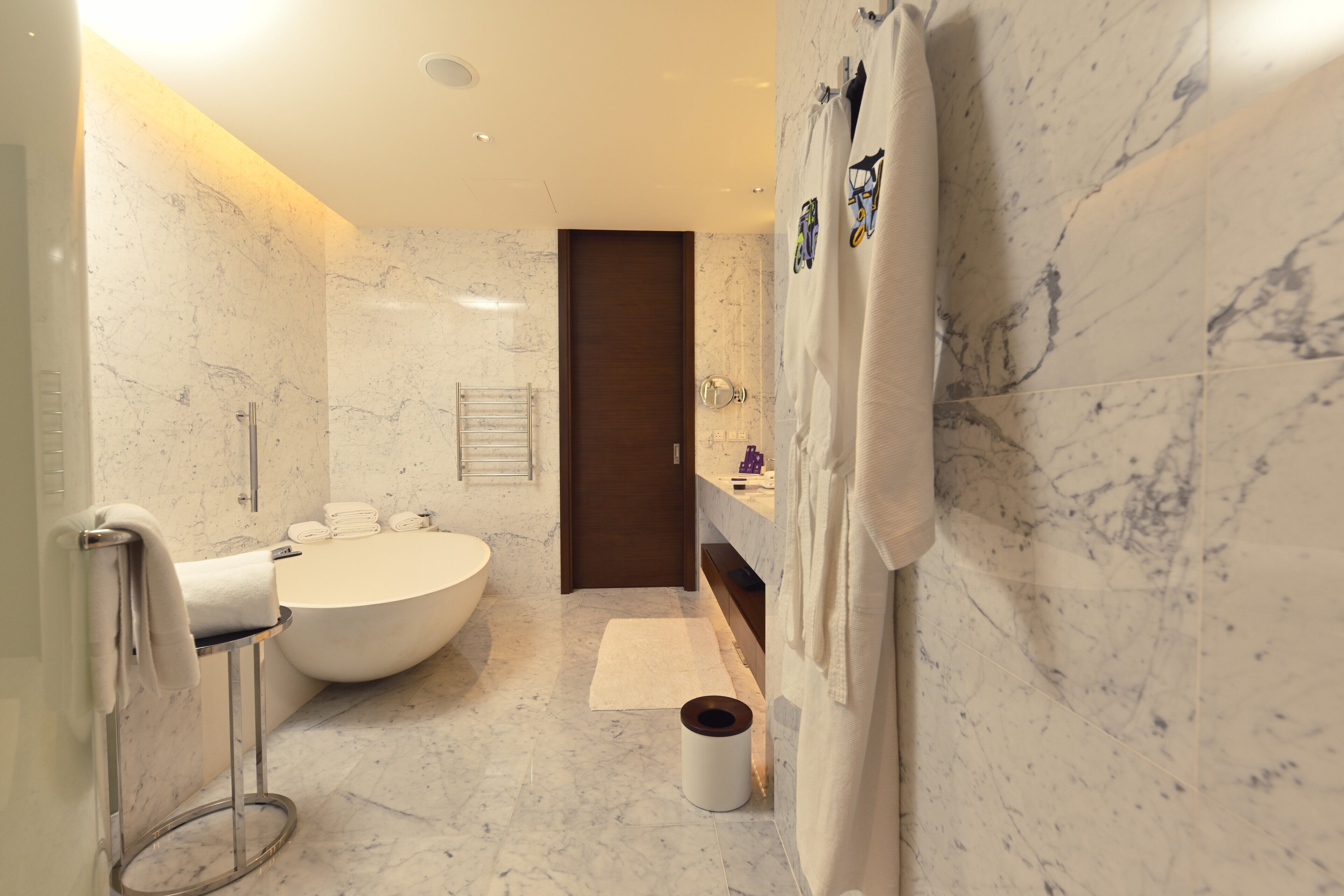 A modern bathroom with a freestanding bathtub, a large mirror, and a marble wall.