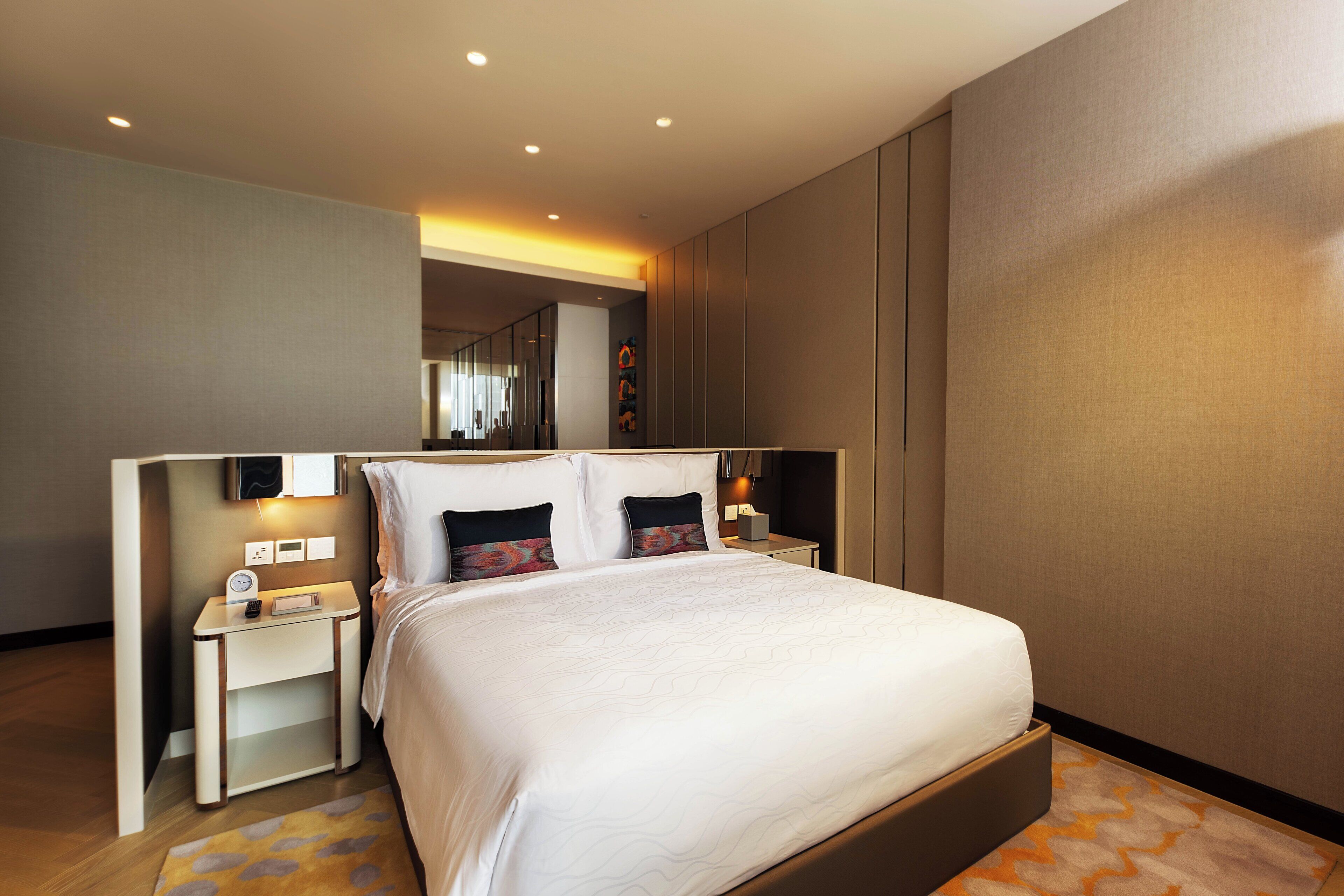 A modern hotel room with a large bed, bedside tables, and a nightstand with a lamp.