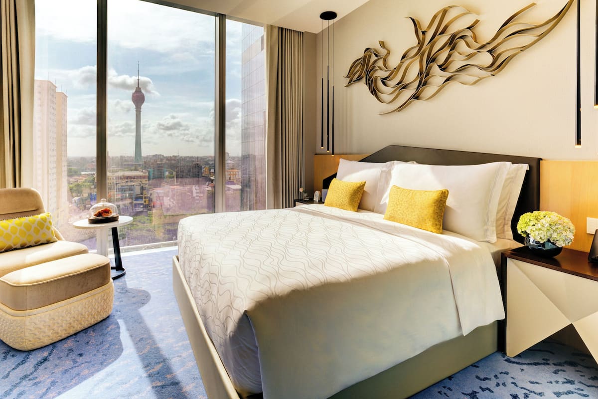 Camera d'albergo con un letto grande, una sedia, un comodino e vista sulla città, inclusa una torre.