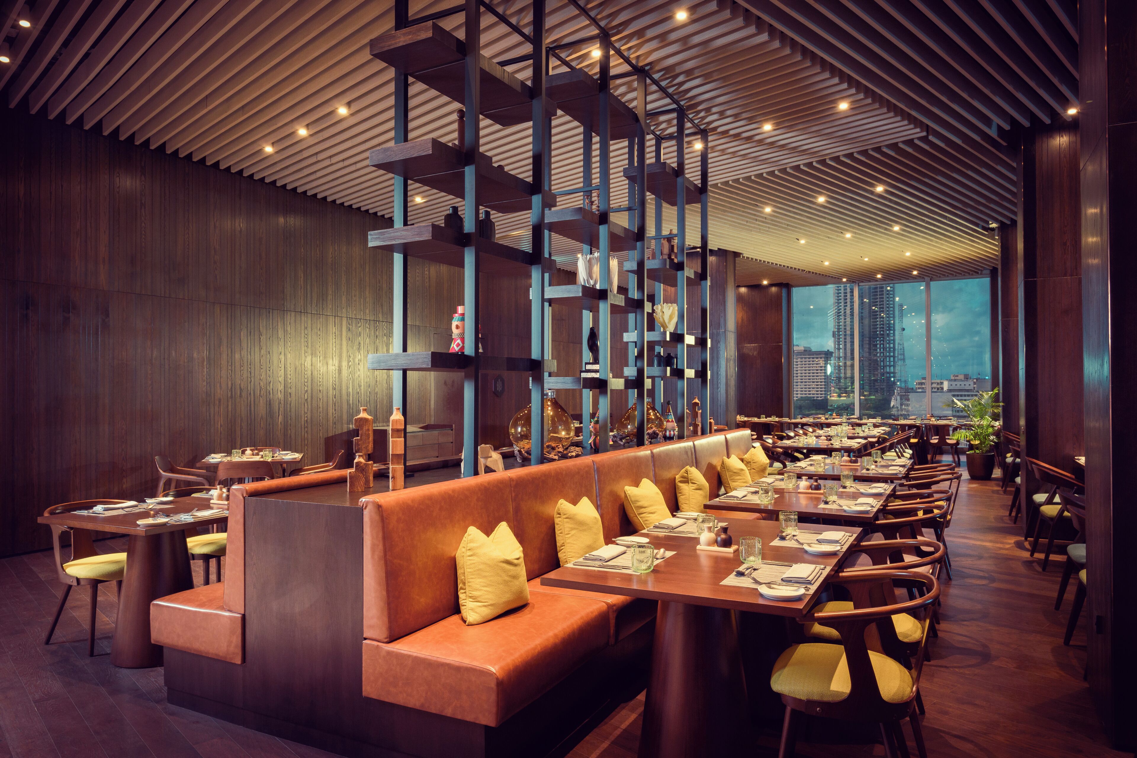 A modern restaurant with a long counter, booths, and a city view.