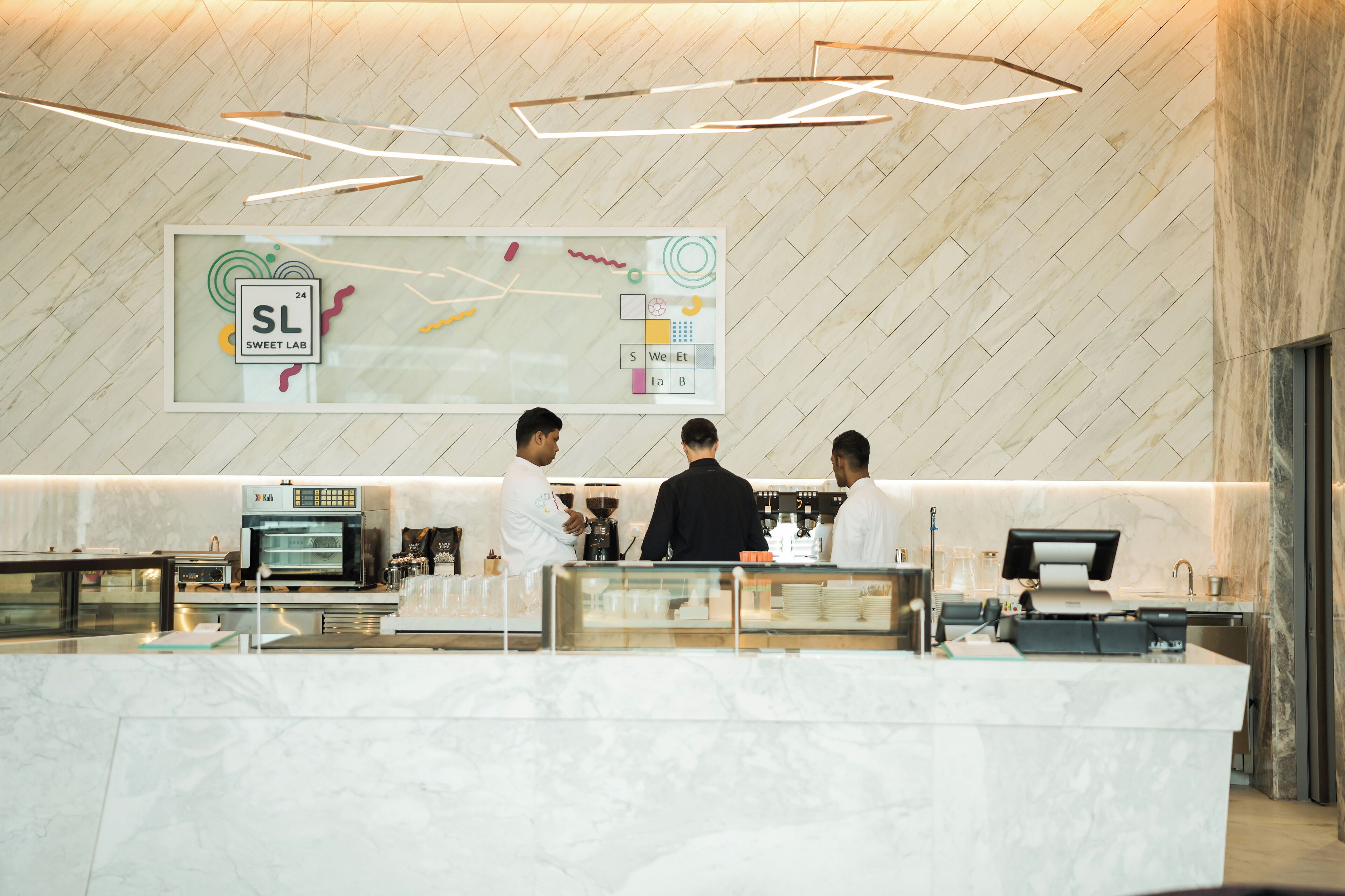 L’intérieur d’un café moderne, avec un comptoir en marbre, un grand panneau affichant le menu et une machine à café.
