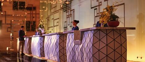 A reception area with a modern design, featuring a long reception desk with geometric patterns and a potted plant.