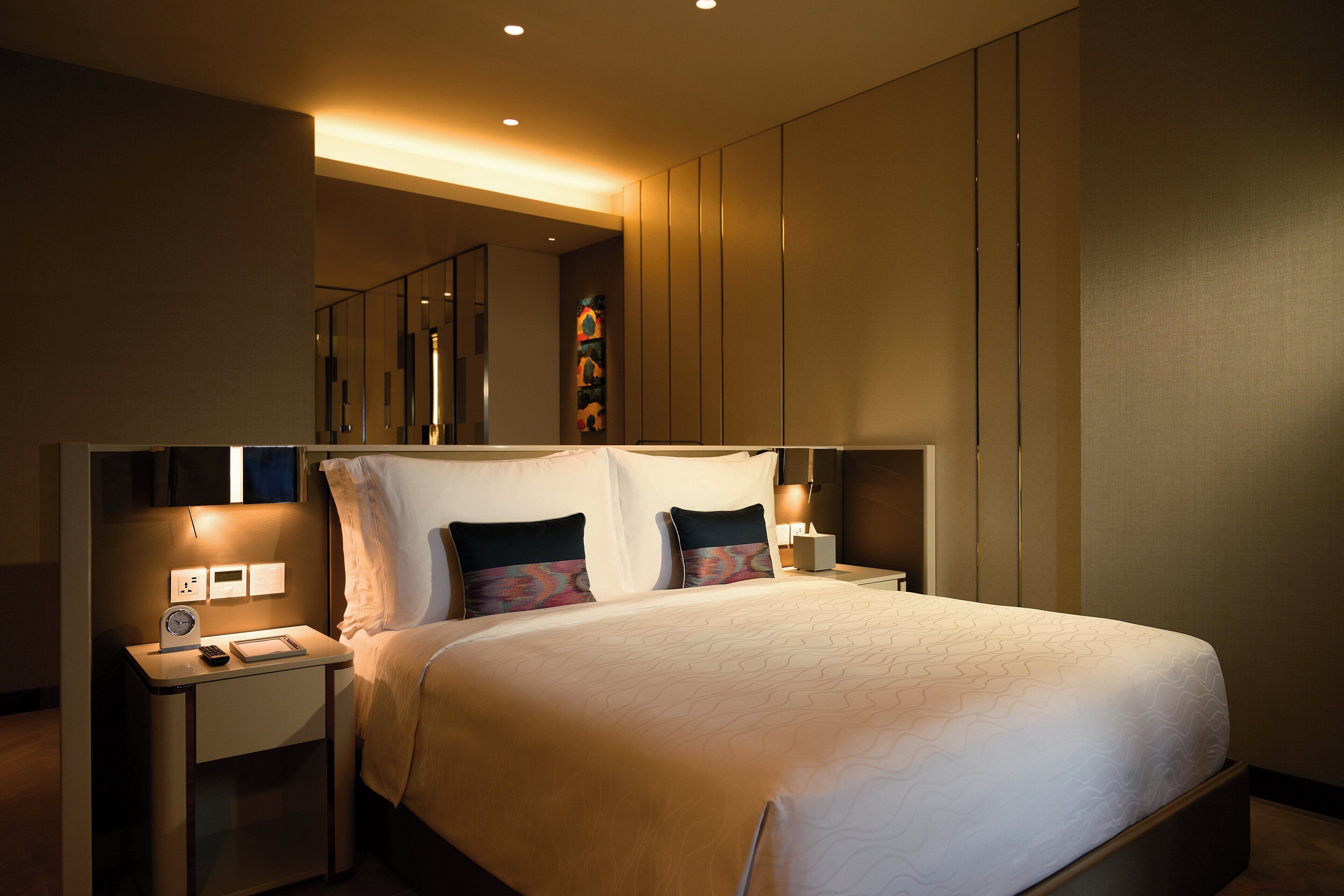 A hotel room with a large bed, bedside tables, a nightstand, and a wall-mounted TV.