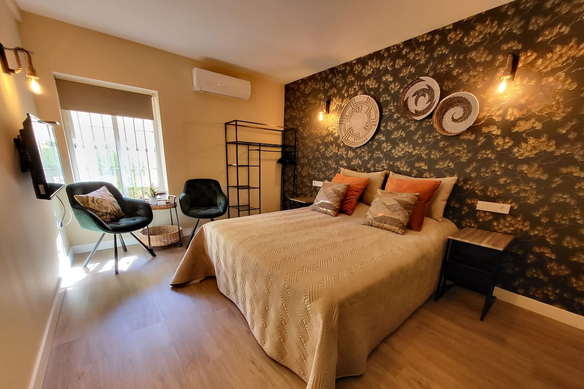 Een slaapkamer met een groot bed, twee stoelen, een tafeltje en een televisie aan de muur.