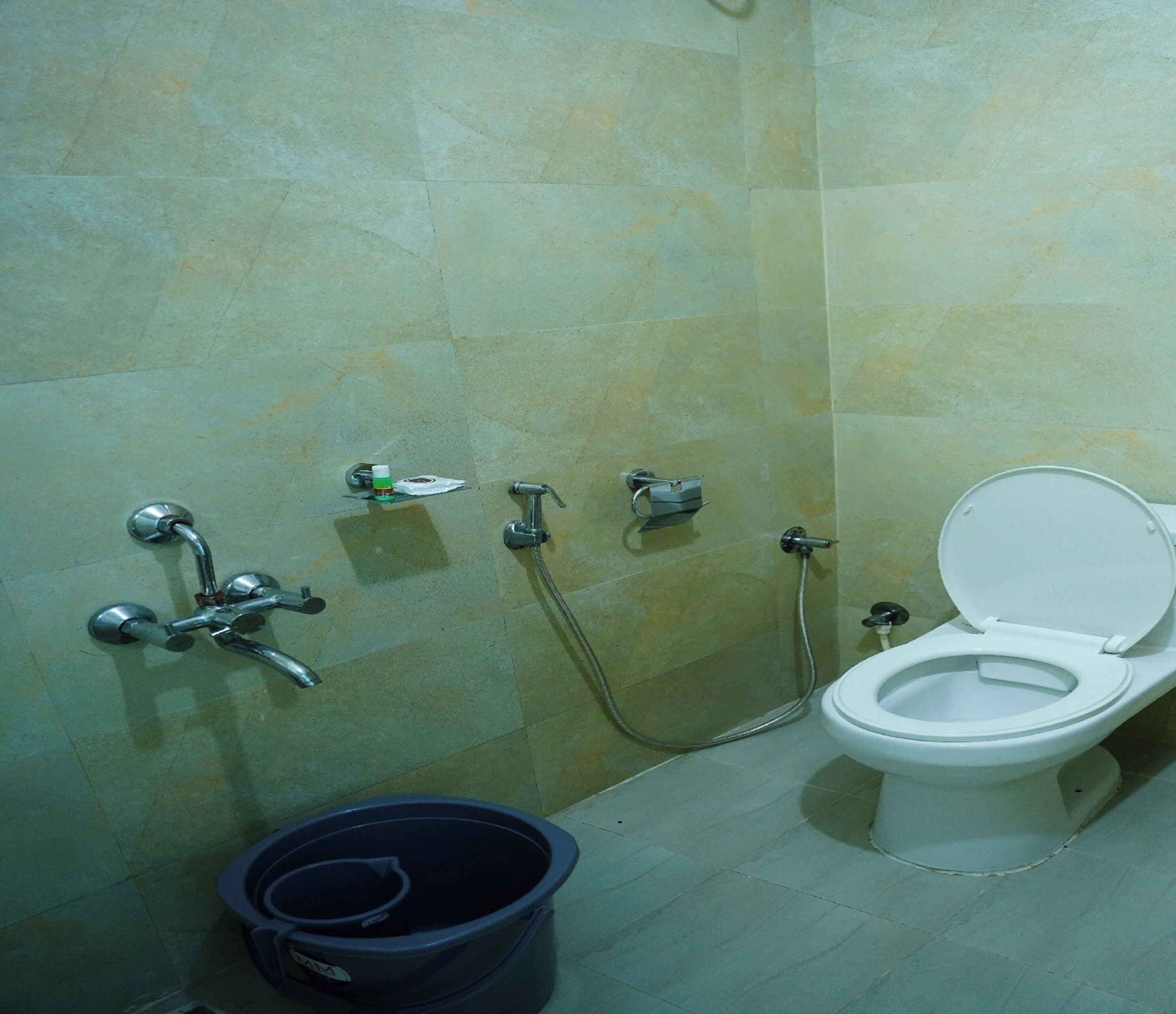 A bathroom with a toilet, a shower, and a bucket.