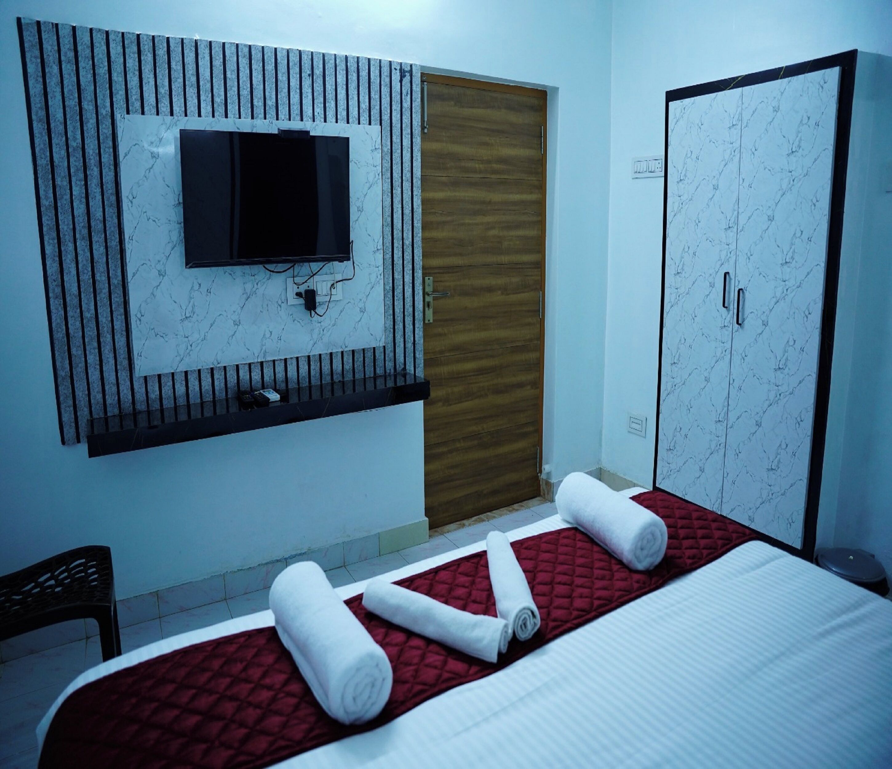 A hotel room with a bed, a TV mounted on a marble wall, a wooden door, and a wardrobe with a marble pattern.