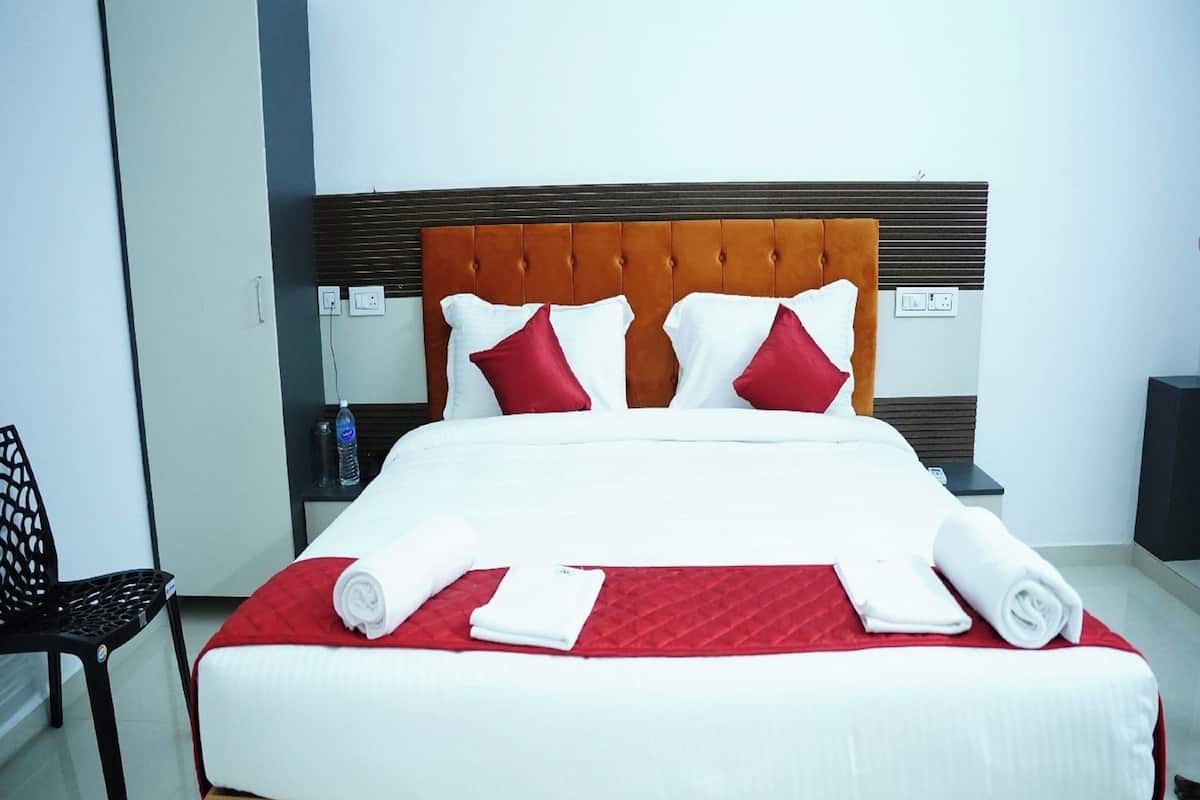 A neatly made bed with white and red bedding, a wooden headboard, and a red accent pillow. There is a black chair and a white wardrobe in the room.