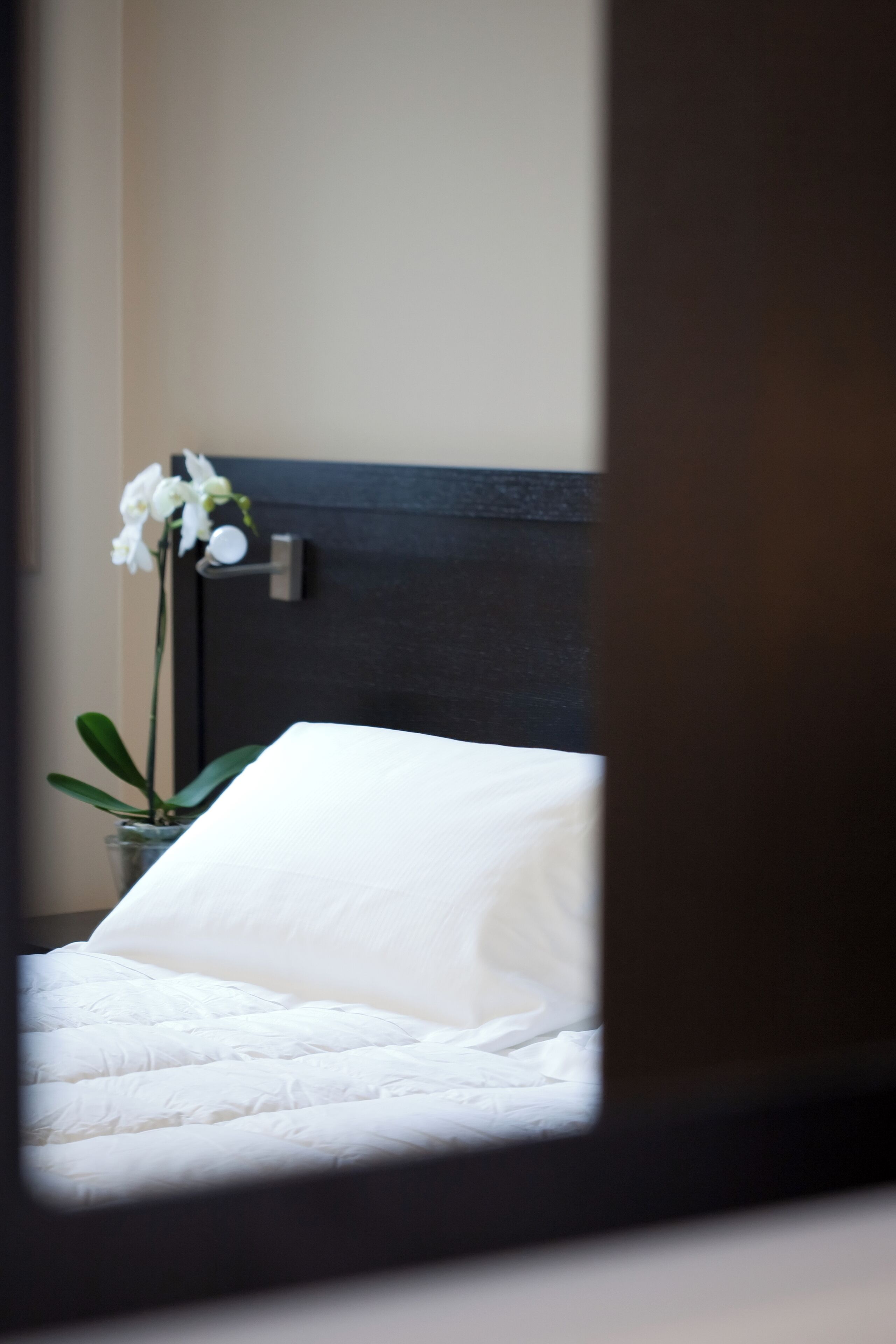 Una cama con ropa de cama blanca y una orquídea en maceta.
