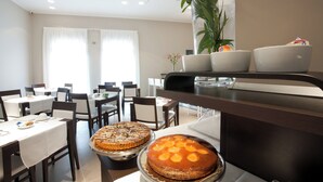 A dining area with tables, chairs, and a large plant. - Mosaico Suite (Cesena)