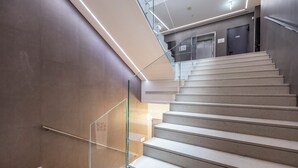 A modern staircase with glass railings and a handrail, leading to an upper level. - Mosaico Suite (Cesena)
