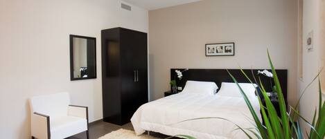 A modern bedroom with a large bed, a chair, a wardrobe, and a mirror.