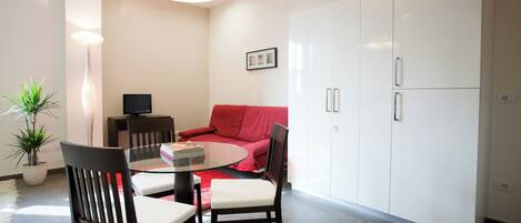 Una sala de estar moderna con una mesa de comedor de vidrio, dos sillas, un sofá rojo, un televisor y un mueble.