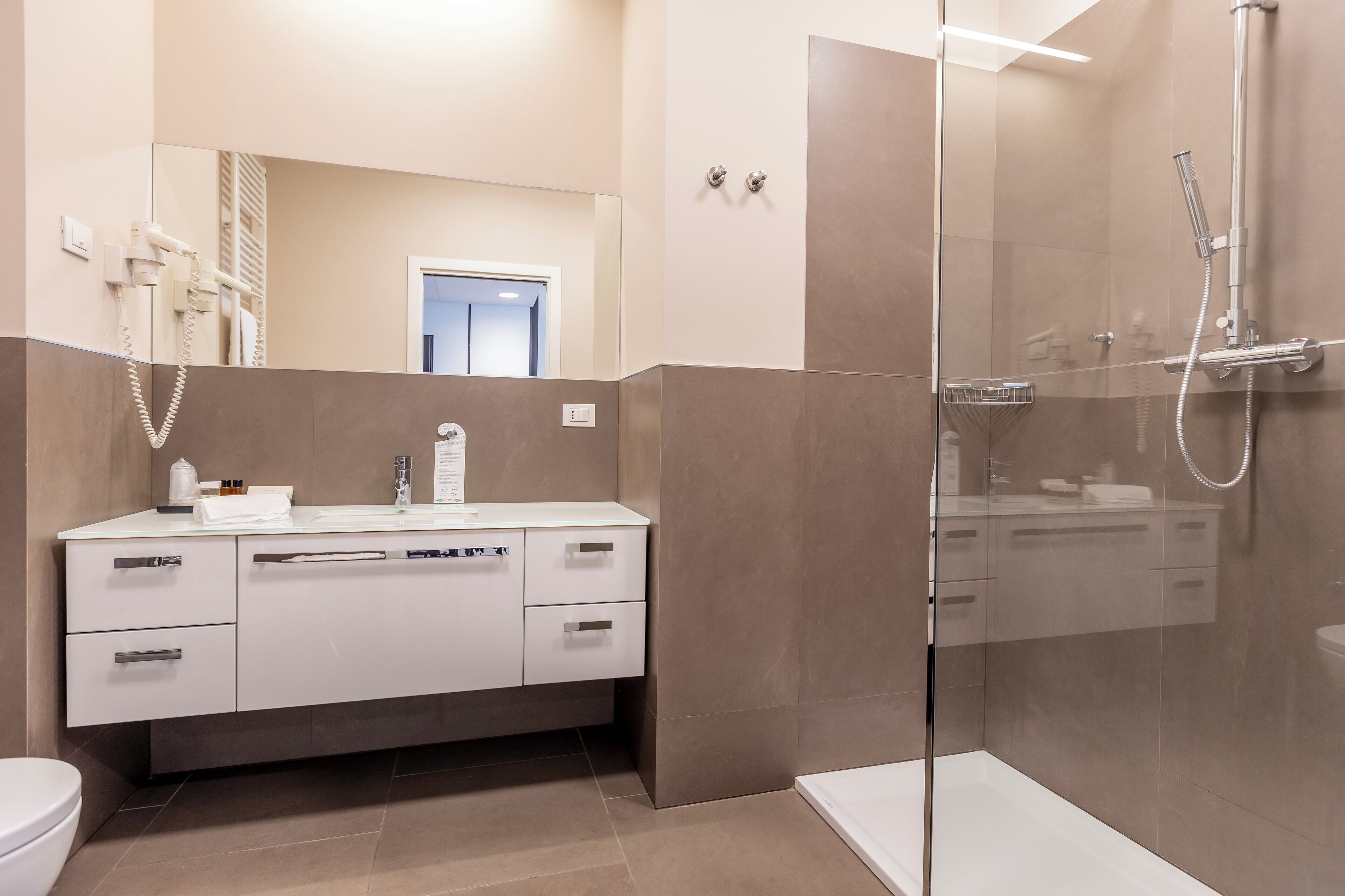 Un baño moderno con cabina de ducha de vidrio, tocador blanco con espejo y un inodoro.