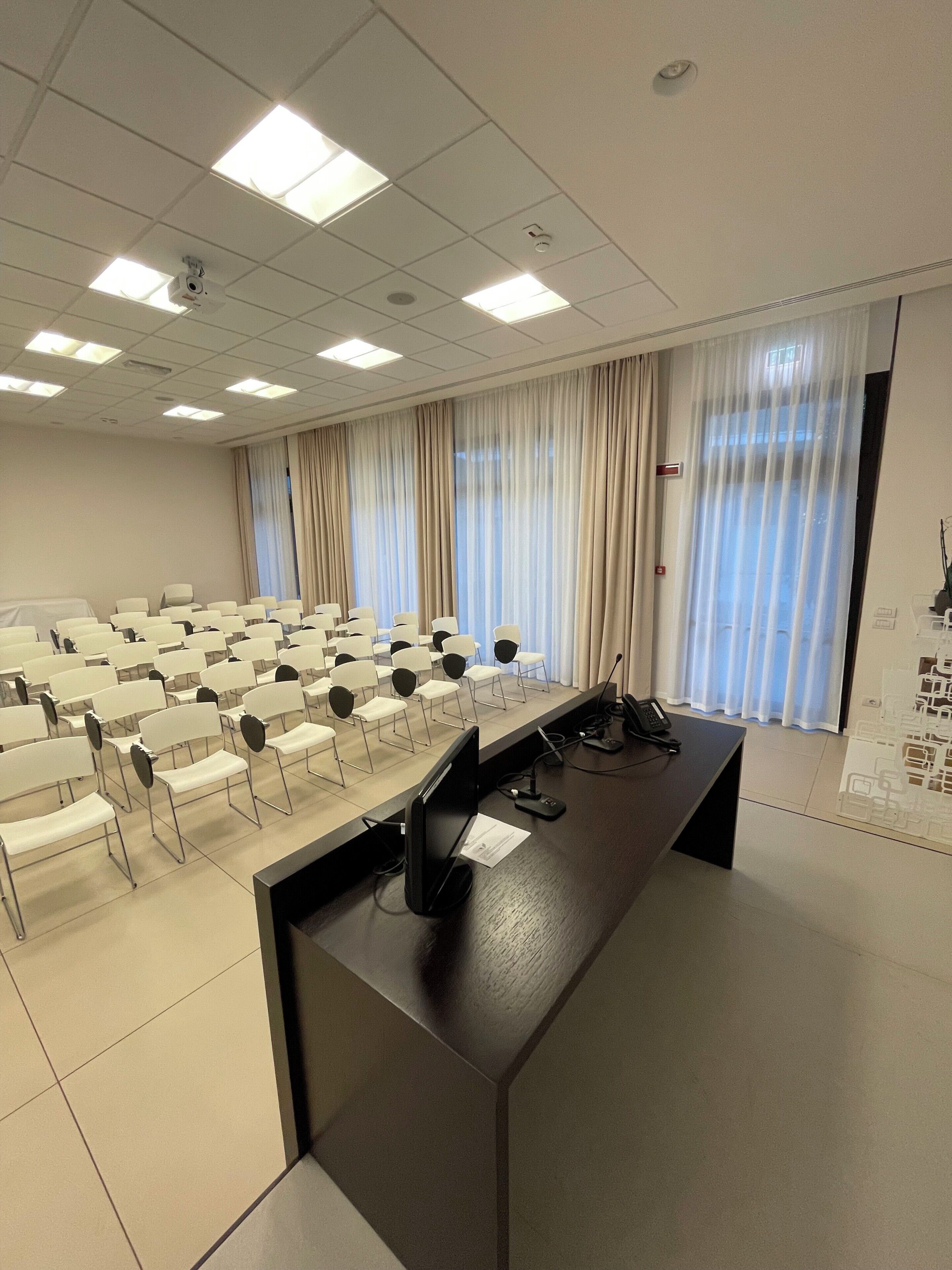 A conference room with rows of chairs, a podium, and a large window with curtains.