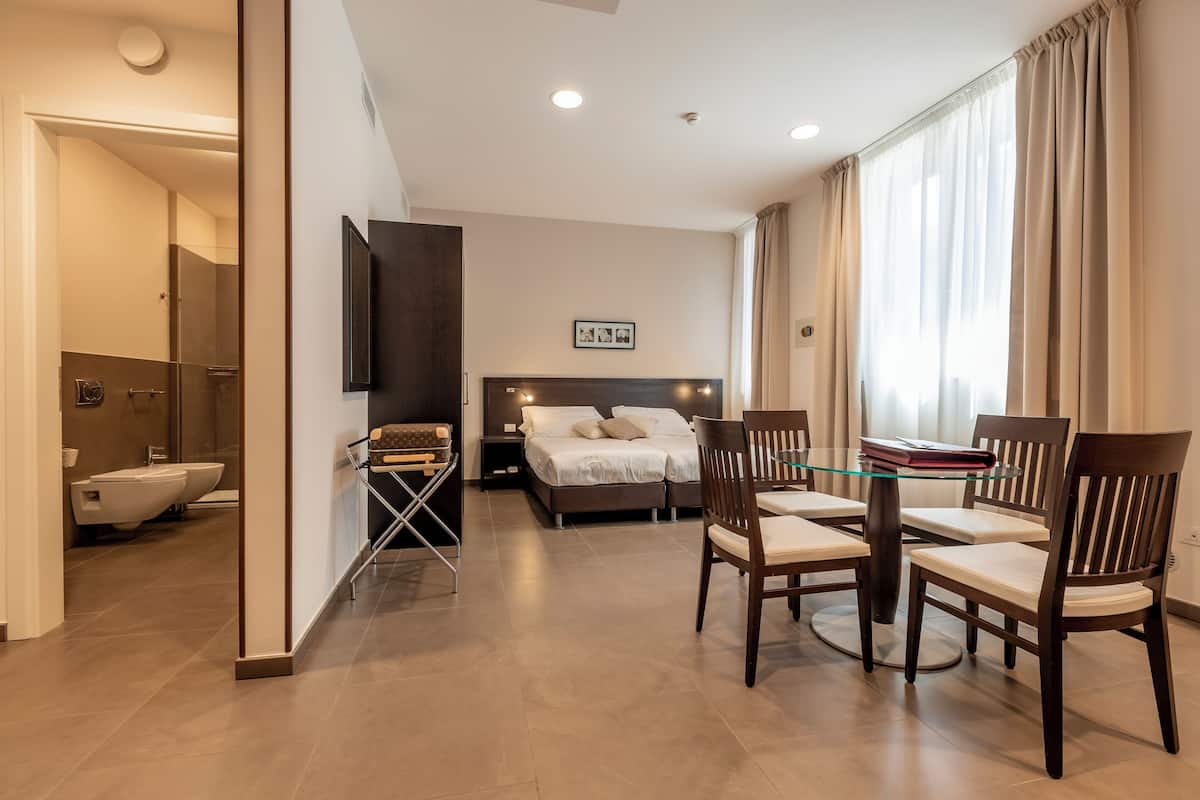 Ein Hotelzimmer mit Bett, Nachttisch und Esstisch mit Glasplatte und Stühlen.