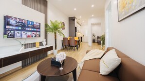 Un salon moderne avec un téléviseur à écran plat fixé au mur, un canapé marron, une table basse ronde et un coin repas comprenant une petite table et des chaises.