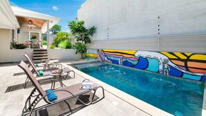 Une piscine avec des chaises longues et une fresque murale sur le mur adjacent.