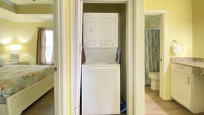 Ein kleines Hotelzimmer mit Bett, Waschmaschine, kleinem Badezimmer und Deckenventilator.