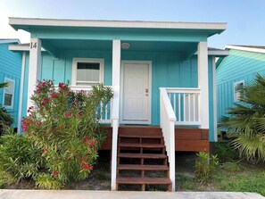 A two-story house with a front porch, a white door, and a staircase leading to the entrance. - This house is a 2 bedroom(s), 1 bathrooms, located in Rockport, TX. (Rockport)