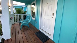 A turquoise porch with two Adirondack chairs, a white door, and a small welcome mat.