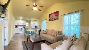 A living room with a sofa, coffee table, and a ceiling fan. There is a dining area with a table and chairs.