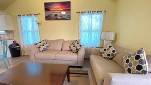 A living room with a sofa set, a wooden coffee table, and a painting of a sunset.
