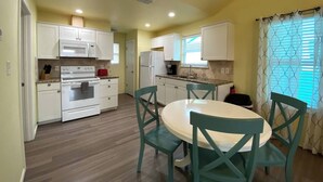 A compact kitchen with white cabinets, a microwave, a stove, and a refrigerator. There is a dining table with four chairs.