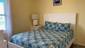Un dormitorio con cama, mesita de noche, lámpara y un cuadro en la pared.