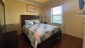 Ein Schlafzimmer mit einem Bett, einem Deckenventilator, einem Fenster mit Jalousien und einem gerahmten Bild an der Wand.
